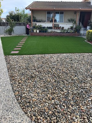 San Jose Ca - The image shows the front yard of a residential home with a clean, modern landscaping design.
In the foreground, there is a large area covered with river rock, creating a low-maintenance and natural look. Behind it, there is a rectangular section of green artificial turf, professionally installed and well leveled. A decorative walkway made of red rectangular pavers runs across the turf, leading toward the porch. San Jose Ca - The image shows the front yard of a residential home with a clean, modern landscaping design.
In the foreground, there is a large area covered with river rock, creating a low-maintenance and natural look. Behind it, there is a rectangular section of green artificial turf, professionally installed and well leveled. A decorative walkway made of red rectangular pavers runs across the turf, leading toward the porch.