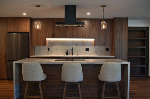 Warm Wood Kitchen Remodel | Elevate Builders Hawaii - This Oahu kitchen remodel was designed with warm wood cabinetry, soft lighting, matte black fixtures, and stone surfaces that bring a calm, grounded feeling into the home. The large island creates a comfortable place for cooking, gathering, and everyday living, while the custom storage keeps the space refined and practical. Warm Wood Kitchen Remodel | Elevate Builders Hawaii - This Oahu kitchen remodel was designed with warm wood cabinetry, soft lighting, matte black fixtures, and stone surfaces that bring a calm, grounded feeling into the home. The large island creates a comfortable place for cooking, gathering, and everyday living, while the custom storage keeps the space refined and practical.