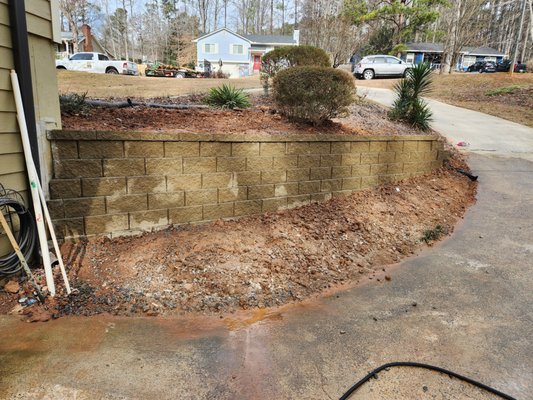 Retaining Wall Rescue - This property had a retaining wall that had completely failed due to improper installation, poor base preparation, and a lack of drainage behind the structure. The existing wall was leaning, separating, and collapsing in several sections, which created safety concerns and ongoing soil erosion. Water was collecting behind the wall with no place to drain, causing pressure to build up and push the blocks outward.
Arterra Outdoors began by carefully removing the damaged wall and excavating the area to expose the source of the problem. We removed all compromised materials, cleared out the washed-out soil, and addressed the drainage issues that caused the failure. Once the site was properly prepped, we installed a new compacted gravel base to ensure long-term stability and prevent future settling.
To solve the water pressure problem, we integrated a full drainage system behind the new wall, including perforated pipe, gravel backfill, and geotextile fabric to prevent soil migration. This allows water to escape safely and keeps the structure strong over time.
For the rebuild, we used high-quality Belgard retaining wall blocks, chosen for their durability, interlocking strength, and clean appearance. Each course was leveled, locked, and backfilled correctly to meet structural standards and create a long-lasting solution. The final result is a stronger, cleaner, and professionally engineered retaining wall that protects the property, stabilizes the hillside, and adds curb appeal.
This project is a great example of how replacing a failing wall with a properly engineered system can completely transform both the safety and the look of a yard. Arterra Outdoors ensures every wall is built to last—never cutting corners and always installing the drainage and foundation needed for long-term performance. Retaining Wall Rescue - This property had a retaining wall that had completely failed due to improper installation, poor base preparation, and a lack of drainage behind the structure. The existing wall was leaning, separating, and collapsing in several sections, which created safety concerns and ongoing soil erosion. Water was collecting behind the wall with no place to drain, causing pressure to build up and push the blocks outward.
Arterra Outdoors began by carefully removing the damaged wall and excavating the area to expose the source of the problem. We removed all compromised materials, cleared out the washed-out soil, and addressed the drainage issues that caused the failure. Once the site was properly prepped, we installed a new compacted gravel base to ensure long-term stability and prevent future settling.
To solve the water pressure problem, we integrated a full drainage system behind the new wall, including perforated pipe, gravel backfill, and geotextile fabric to prevent soil migration. This allows water to escape safely and keeps the structure strong over time.
For the rebuild, we used high-quality Belgard retaining wall blocks, chosen for their durability, interlocking strength, and clean appearance. Each course was leveled, locked, and backfilled correctly to meet structural standards and create a long-lasting solution. The final result is a stronger, cleaner, and professionally engineered retaining wall that protects the property, stabilizes the hillside, and adds curb appeal.
This project is a great example of how replacing a failing wall with a properly engineered system can completely transform both the safety and the look of a yard. Arterra Outdoors ensures every wall is built to last—never cutting corners and always installing the drainage and foundation needed for long-term performance.