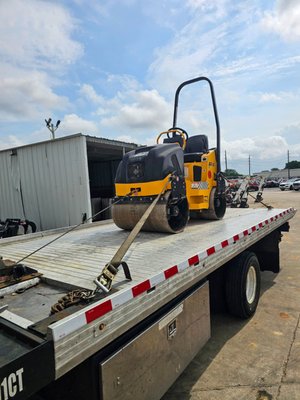 Construction Equipment Towing - Heavy road roller securely strapped and transported using professional flatbed towing for construction equipment and a Bobcat mini excavator safely loaded and hauled on a flatbed for reliable heavy equipment transport.