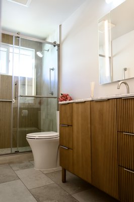 Modern bath remodel - This modern bathroom features warm wood-textured shower walls, a sleek glass enclosure, and soft neutral tones that create a calm, spa-like atmosphere. The vanity combines vertical-grain cabinetry with a bright marble countertop, while brushed metal fixtures add clean, contemporary detail to the streamlined design. Modern bath remodel - This modern bathroom features warm wood-textured shower walls, a sleek glass enclosure, and soft neutral tones that create a calm, spa-like atmosphere. The vanity combines vertical-grain cabinetry with a bright marble countertop, while brushed metal fixtures add clean, contemporary detail to the streamlined design.