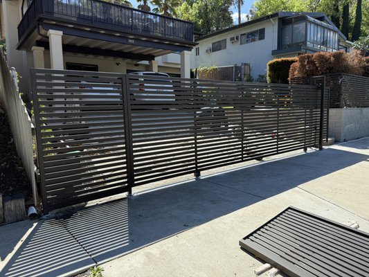 Complete Gate & Fence Replacement – Modern Horizontal Steel System - Woodland Hills - This customer reached out to us because their existing gate and fence were heavily rusted, sagging, and no longer secure. The old system had multiple structural issues, uneven panels, and failing hardware that made daily use difficult and unsafe.
What We Did
We removed the entire outdated iron gate and fencing and replaced it with a brand-new modern horizontal steel system. The upgrade included:
Custom-fabricated sliding gate designed for the steep driveway
New pedestrian access gate with a digital keypad lock
Matching horizontal steel fence panels for a clean, contemporary look
Fresh steel track, posts, and reinforced footing for proper alignment and long-term stability
Beautiful bronze-matte powder-coated finish for maximum durability and weather resistance
The Result
The new gate system completely transformed the property. It’s now:
Strong, secure, and smooth-operating
Modern and visually clean
Fully aligned with zero sagging or scraping
Built for long-term performance with minimal maintenance
Another beautiful upgrade for a very happy homeowner — and a night-and-day difference from the original system.
If you’re looking to repair or replace your driveway gate, sliding gate, or fence, Clearway delivers high-quality fabrication and installation across the Pasadena and surrounding areas. Complete Gate & Fence Replacement – Modern Horizontal Steel System - Woodland Hills - This customer reached out to us because their existing gate and fence were heavily rusted, sagging, and no longer secure. The old system had multiple structural issues, uneven panels, and failing hardware that made daily use difficult and unsafe.
What We Did
We removed the entire outdated iron gate and fencing and replaced it with a brand-new modern horizontal steel system. The upgrade included:
Custom-fabricated sliding gate designed for the steep driveway
New pedestrian access gate with a digital keypad lock
Matching horizontal steel fence panels for a clean, contemporary look
Fresh steel track, posts, and reinforced footing for proper alignment and long-term stability
Beautiful bronze-matte powder-coated finish for maximum durability and weather resistance
The Result
The new gate system completely transformed the property. It’s now:
Strong, secure, and smooth-operating
Modern and visually clean
Fully aligned with zero sagging or scraping
Built for long-term performance with minimal maintenance
Another beautiful upgrade for a very happy homeowner — and a night-and-day difference from the original system.
If you’re looking to repair or replace your driveway gate, sliding gate, or fence, Clearway delivers high-quality fabrication and installation across the Pasadena and surrounding areas.