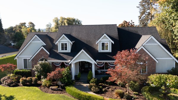 Classic Colonial Elegance - Composite Roof Replacement in Puyallup, WA - Type of Project: Residential roof replacement for a large home and detached garage with an ADU (Accessory Dwelling Unit).
Scope: This expansive project involved replacing 103 total squares of roofing on the primary residence and an ADU. The roof design featured 34 separate roof facets, with a predominant pitch of 9/12 and several steeper sections with 10/12 and 12/12 pitches. These multiple slope transitions and architectural details, such as doghouse dormers, contributed to the complexity and intricacy of the project.
Location & Climate Considerations: Situated in the Pacific Northwest, this property required a roof that could handle the region’s frequent rain, high winds, and varying weather patterns. Careful material selection and expert installation were essential to ensure durability and aesthetic harmony.
Craftsmanship: The roof has 34 facets of varying pitches, requiring superior expertise and precision. Valentine Roofing’s skilled roofing crew meticulously planned and executed each facet installation, ensuring seamless transitions between different slopes and angles. The steep pitches and architectural elements, such as doghouse dormers, were particularly challenging and demanded custom flashing and detailed shingle placement to ensure proper water drainage and a cohesive look. Classic Colonial Elegance - Composite Roof Replacement in Puyallup, WA - Type of Project: Residential roof replacement for a large home and detached garage with an ADU (Accessory Dwelling Unit).
Scope: This expansive project involved replacing 103 total squares of roofing on the primary residence and an ADU. The roof design featured 34 separate roof facets, with a predominant pitch of 9/12 and several steeper sections with 10/12 and 12/12 pitches. These multiple slope transitions and architectural details, such as doghouse dormers, contributed to the complexity and intricacy of the project.
Location & Climate Considerations: Situated in the Pacific Northwest, this property required a roof that could handle the region’s frequent rain, high winds, and varying weather patterns. Careful material selection and expert installation were essential to ensure durability and aesthetic harmony.
Craftsmanship: The roof has 34 facets of varying pitches, requiring superior expertise and precision. Valentine Roofing’s skilled roofing crew meticulously planned and executed each facet installation, ensuring seamless transitions between different slopes and angles. The steep pitches and architectural elements, such as doghouse dormers, were particularly challenging and demanded custom flashing and detailed shingle placement to ensure proper water drainage and a cohesive look.