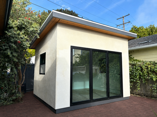 La Jolla - Home Office Shed - Tan stucco shed, built as a home office for an owner who ran out of space in the house. Site-built shell, drywalled and insulated inside, black-framed slider for the light, vinyl plank on the floor.
The insulation and drywall are what turn a shed into a room — most kit sheds don't have a wall cavity built for it. La Jolla - Home Office Shed - Tan stucco shed, built as a home office for an owner who ran out of space in the house. Site-built shell, drywalled and insulated inside, black-framed slider for the light, vinyl plank on the floor.
The insulation and drywall are what turn a shed into a room — most kit sheds don't have a wall cavity built for it.