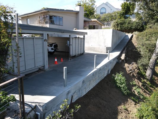 76-foot Retaining Wall with a Cantilevered Ramp and a Slab Foundation - We engineered and built a 76-foot retaining wall with a cantilevered ramp and a solid slab foundation, all supported by 7 sturdy piles. The project began by removing the railroad tie wall and flattening the area. We then dug the piles, set rebar, and applied shotcrete to form the wall, followed by pouring the slab.

At the foot of the eastern wall, we extended and waterproofed the area to seamlessly integrate a planter, while ensuring efficient drainage by installing a subdrain system. Finally, we backfilled and compacted the wall, bringing this project to completion!