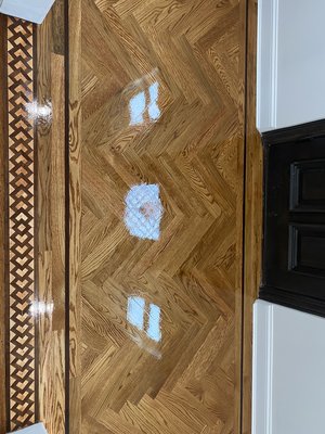 White oak herringbone install and finish with custom inlay saddle. - The foyer was initially tiled; however, the owner desired a consistent wooden appearance throughout. Consequently, we removed the tiles, applied Bona R540 moisture barrier to seal the plywood, and proceeded to install a herringbone floor. This floor featured a walnut and white oak straight plank border, complemented by a mixture of gunstock and early American stains. To protect the floor during the waiting period for the inlay saddle, we applied one coat of polyurethane. Upon its delivery, the inlay saddle was installed, stained, and finished with an oil-based polyurethane.
