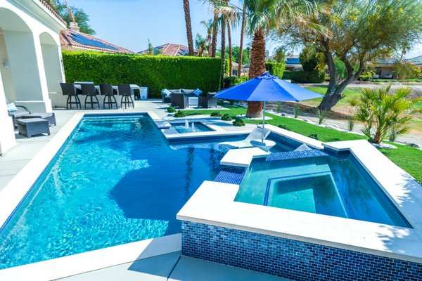 Rancho Mirage Country Club Pool & Spa Build - Build a pool behind a Rancho Mirage country club home and the bar is already set. The fairway behind it is manicured every morning. The mountain line is non-negotiable. The home is Mediterranean revival with an arched colonnade, barrel-tile roof, stucco soft as a sandstorm, and anything you put in the backyard has to earn its place against it.
This one earned it.
A geometric modern pool laid out in clean rectilinear lines, edged in crisp white travertine that stays walkable when the deck hits triple digits. A wide Baja shelf sits just below the surface, fitted with an in-pool umbrella sleeve and twin loungers, you know the kind of detail snowbirds notice and locals expect. Two deck jets arc up from a sun-shelf overflow and spill clean into the main basin. The raised spa is wrapped corner-to-corner in cobalt and teal glass mosaic that catches the late-afternoon sun like cut sapphires from anywhere on the deck.
The details keep landing. The waterline runs a graduated blue blend, deeper cobalt at the base, lighter teal up top that reads as one color from across the patio and three from the edge. A custom mosaic medallion anchors the floor of the tanning shelf. The interior finish is a quartz blend that pulls true tropical blue out of the water even in flat midday light. From the great-room sliders, the spa spillover, the palms, and the fairway stack into one uninterrupted view of Rancho Mirage at its best.
Here's the part most builders won't put in writing: a pool like this only stays this clean if somebody keeps it this clean. The Coachella Valley is brutal on equipment; UV cooks controllers, hard water scales heaters, and the wind off the fairway finds every skimmer basket from Mission Hills to Tamarisk.
Desert Luxury Pools designed, permitted, built, and now services this pool year-round. Same crew that set every tile knows every valve and every setting on the variable-speed pump. No handoffs. No "call the warranty department." Just one local team treating it like their own, every service day, every season, year five and beyond. Rancho Mirage Country Club Pool & Spa Build - Build a pool behind a Rancho Mirage country club home and the bar is already set. The fairway behind it is manicured every morning. The mountain line is non-negotiable. The home is Mediterranean revival with an arched colonnade, barrel-tile roof, stucco soft as a sandstorm, and anything you put in the backyard has to earn its place against it.
This one earned it.
A geometric modern pool laid out in clean rectilinear lines, edged in crisp white travertine that stays walkable when the deck hits triple digits. A wide Baja shelf sits just below the surface, fitted with an in-pool umbrella sleeve and twin loungers, you know the kind of detail snowbirds notice and locals expect. Two deck jets arc up from a sun-shelf overflow and spill clean into the main basin. The raised spa is wrapped corner-to-corner in cobalt and teal glass mosaic that catches the late-afternoon sun like cut sapphires from anywhere on the deck.
The details keep landing. The waterline runs a graduated blue blend, deeper cobalt at the base, lighter teal up top that reads as one color from across the patio and three from the edge. A custom mosaic medallion anchors the floor of the tanning shelf. The interior finish is a quartz blend that pulls true tropical blue out of the water even in flat midday light. From the great-room sliders, the spa spillover, the palms, and the fairway stack into one uninterrupted view of Rancho Mirage at its best.
Here's the part most builders won't put in writing: a pool like this only stays this clean if somebody keeps it this clean. The Coachella Valley is brutal on equipment; UV cooks controllers, hard water scales heaters, and the wind off the fairway finds every skimmer basket from Mission Hills to Tamarisk.
Desert Luxury Pools designed, permitted, built, and now services this pool year-round. Same crew that set every tile knows every valve and every setting on the variable-speed pump. No handoffs. No "call the warranty department." Just one local team treating it like their own, every service day, every season, year five and beyond.