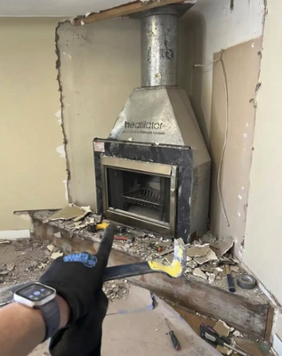 Metal chimney system - This project was a complete floor-to-ceiling fireplace renovation that transformed a corner hearth. It started with a demolition phase where the existing wall structure was stripped away down to the bare framing to expose the fireplace unit and internal flue pipe. Afterward, the wall was rebuilt and finished with a textured, cream-colored stone veneer that runs all the way to the ceiling, creating a bright and modern rustic accent wall. The final look neatly contrasts this new light stone facade with the original dark stone ledge left at the base.