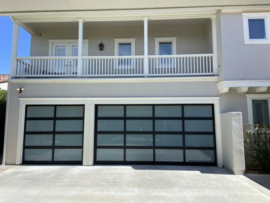 FULL VIEW ALUMINUM GLASS DOORS - Replace your old wooden doors with full view aluminum glass doors. This frosted glass and black aluminum-frame garage door is a showstopper. Designed for a luxury residence, it provides full privacy from the outside while allowing light diffusion inside. The client requested a minimalist, modern look, and this custom install hit the mark. Paired with a whisper-quiet wall-mounted opener and motion lighting for added convenience. FULL VIEW ALUMINUM GLASS DOORS - Replace your old wooden doors with full view aluminum glass doors. This frosted glass and black aluminum-frame garage door is a showstopper. Designed for a luxury residence, it provides full privacy from the outside while allowing light diffusion inside. The client requested a minimalist, modern look, and this custom install hit the mark. Paired with a whisper-quiet wall-mounted opener and motion lighting for added convenience.