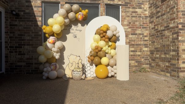 Winnie the Pooh Inspired Themed Baby Shower - It started with a simple message from a mom-to-be:
“I grew up reading Winnie the Pooh with my dad. I want my baby to grow up with that same warmth.”
That one sentence shaped the entire design.
Instead of going overly cartoonish, we leaned into the soft, nostalgic Hundred Acre Wood feel — warm honey tones, muted pastels, soft creams, and delicate florals that felt like they were gently blooming in a quiet forest morning.
The backdrop panels were custom painted in a warm beige palette to mimic storybook parchment. We paired them with a fluted pedestal to display the cake — representing Pooh’s beloved “hunny pot” — and layered floral arrangements that felt organic, almost as if they were gathered by Piglet himself.
Custom vinyl lettering was added in a soft handwritten script to give it that classic children’s book charm.
The goal wasn’t just to create a photo backdrop.
It was to create a moment where guests stepped into a childhood memory.

When the mom walked in and teared up seeing it fully set — that’s when we knew we got it right.

The space felt gentle, joyful, and timeless. Just like Winnie the Pooh which was inspired based upon on.