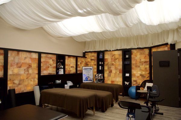 Physical Therapy Room - This is our physical therapy room, also known as the salt room. It is equipped with a variety of tables and equipment for patients to be able to productively perform their stretches in a comfy, calming space. The room is spacious with ambient lighting, and has an additional entryway into the chiropractic room which is tailored for adjustments.