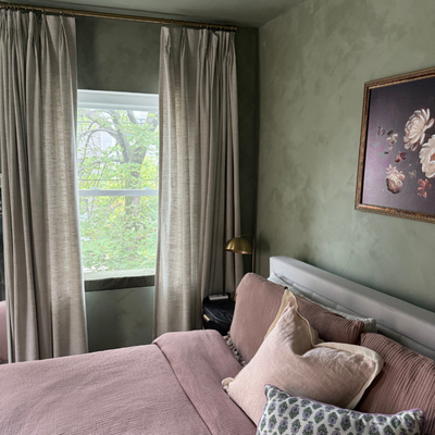 Elegant Bedroom Refresh with Soft Drapery and Earthy Hues - "This home project centers around a sophisticated window treatment upgrade that enhances the ambiance, functionality, and overall design of the bedroom. The focal point is a pair of custom full-length drapes installed on brass curtain rods mounted just below the ceiling—drawing the eye upward and giving the modestly sized room an immediate sense of height and elegance.The curtains themselves are made from a soft, subtly textured fabric in a neutral greige tone. This choice balances beautifully with the olive-toned, plaster-effect walls, introducing a soft contrast without disrupting the serene, earthy palette. The drapes are lined, offering both light filtration and privacy depending on the desired atmosphere. Whether gently parted to let in dappled daylight or drawn fully closed for a cozy cocoon effect, they respond to the room's needs and moods.Each image captures a different state of use:Open: The curtains are pulled to the sides, framing the window and allowing full views of the greenery outside while maintaining an elegant drape with uniform pleats.Partially Closed: This setup allows soft, diffused light into the room, preserving the calm ambiance while reducing glare.Fully Closed: The thick, full fabric shields the room for restful darkness and thermal insulation—ideal for sleep and relaxation.The hardware was chosen with care: brass rods and rings complement the warm metallic tones found elsewhere in the room, including the vintage-style brass bedside lamp. The pleated headers give the drapes a tailored appearance that suits both traditional and transitional styles, aligning seamlessly with the room’s overall aesthetic." Elegant Bedroom Refresh with Soft Drapery and Earthy Hues - "This home project centers around a sophisticated window treatment upgrade that enhances the ambiance, functionality, and overall design of the bedroom. The focal point is a pair of custom full-length drapes installed on brass curtain rods mounted just below the ceiling—drawing the eye upward and giving the modestly sized room an immediate sense of height and elegance.The curtains themselves are made from a soft, subtly textured fabric in a neutral greige tone. This choice balances beautifully with the olive-toned, plaster-effect walls, introducing a soft contrast without disrupting the serene, earthy palette. The drapes are lined, offering both light filtration and privacy depending on the desired atmosphere. Whether gently parted to let in dappled daylight or drawn fully closed for a cozy cocoon effect, they respond to the room's needs and moods.Each image captures a different state of use:Open: The curtains are pulled to the sides, framing the window and allowing full views of the greenery outside while maintaining an elegant drape with uniform pleats.Partially Closed: This setup allows soft, diffused light into the room, preserving the calm ambiance while reducing glare.Fully Closed: The thick, full fabric shields the room for restful darkness and thermal insulation—ideal for sleep and relaxation.The hardware was chosen with care: brass rods and rings complement the warm metallic tones found elsewhere in the room, including the vintage-style brass bedside lamp. The pleated headers give the drapes a tailored appearance that suits both traditional and transitional styles, aligning seamlessly with the room’s overall aesthetic."