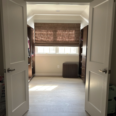 Custom Drapery & Roman Shades Tailored for Every Room - "This project features elegant, full-length pleated drapes in the living room to enhance height and softness, paired with a textured Light Filtering Roman shade in the closet for privacy and warmth—each treatment customized for style and function in its space. The project begins with a walk-in closet outfitted with a beautifully simple and highly functional flat-fold Roman shade. The fabric adds visual interest and warmth to the bright and minimal space. Hung just above a wide, multi-pane window, the shade provides privacy without sacrificing style. Its clean lines suit the angular ceiling, while the soft filtering effect of the material allows for a warm glow to enter the room.This treatment is ideal for spaces that prioritize functionality and subtle sophistication. It controls light effectively and aligns with the clean, built-in millwork on either side of the room, enhancing the structured aesthetic.Living Room — Luxe Full-Length Drapery for a Soaring SpaceThe main living space features vaulted ceilings and expansive windows, and the window treatments are expertly chosen to complement this grandeur. Here, floor-to-ceiling pleated drapes are mounted high and wide on simple black rods, emphasizing verticality and enhancing the architectural height of the room.Each panel is crafted from a soft, light gray fabric with a slight sheen and elegant drape. The color palette seamlessly integrates with the soft neutrals throughout the room—from the dove-gray sectional to the ivory walls and light wood floors. The consistent use of fabric on each window, including the narrower ones flanking the fireplace, creates a cohesive and calming rhythm across the space.These drapes serve a dual purpose:Aesthetic: They frame each window beautifully, softening the strong architectural lines of the space while adding warmth and texture.Functional: They provide light control, especially valuable in a room with a large skylight and southern exposure, helping to reduce glare while preserving the natural brightness of the space.Design Cohesion & Hardware ChoicesA notable strength of this project is the consistency in hardware and fabric choices across different spaces. Matte black curtain rods in the living room provide contrast against the neutral backdrop without feeling heavy. The rods are mounted close to the ceiling line, enhancing the illusion of height and ensuring the drapery stacks back neatly without obstructing views.The Roman Shade and drapery panels use subtly textured fabrics that coordinate without being identical, giving each space its own character while maintaining a unified style. These treatments feel intentional and refined, demonstrating that window coverings are as integral to interior design as furniture or wall finishes.This project is a strong example of how diverse window treatments—when carefully selected and thoughtfully installed—can shape the mood, lighting, and function of a space. From the tailored Roman shade in the closet to the luxurious pleated drapes in the living room, each choice reflects a balance of beauty and practicality. The result is a home that feels cohesive, elevated, and effortlessly comfortable." Custom Drapery & Roman Shades Tailored for Every Room - "This project features elegant, full-length pleated drapes in the living room to enhance height and softness, paired with a textured Light Filtering Roman shade in the closet for privacy and warmth—each treatment customized for style and function in its space. The project begins with a walk-in closet outfitted with a beautifully simple and highly functional flat-fold Roman shade. The fabric adds visual interest and warmth to the bright and minimal space. Hung just above a wide, multi-pane window, the shade provides privacy without sacrificing style. Its clean lines suit the angular ceiling, while the soft filtering effect of the material allows for a warm glow to enter the room.This treatment is ideal for spaces that prioritize functionality and subtle sophistication. It controls light effectively and aligns with the clean, built-in millwork on either side of the room, enhancing the structured aesthetic.Living Room — Luxe Full-Length Drapery for a Soaring SpaceThe main living space features vaulted ceilings and expansive windows, and the window treatments are expertly chosen to complement this grandeur. Here, floor-to-ceiling pleated drapes are mounted high and wide on simple black rods, emphasizing verticality and enhancing the architectural height of the room.Each panel is crafted from a soft, light gray fabric with a slight sheen and elegant drape. The color palette seamlessly integrates with the soft neutrals throughout the room—from the dove-gray sectional to the ivory walls and light wood floors. The consistent use of fabric on each window, including the narrower ones flanking the fireplace, creates a cohesive and calming rhythm across the space.These drapes serve a dual purpose:Aesthetic: They frame each window beautifully, softening the strong architectural lines of the space while adding warmth and texture.Functional: They provide light control, especially valuable in a room with a large skylight and southern exposure, helping to reduce glare while preserving the natural brightness of the space.Design Cohesion & Hardware ChoicesA notable strength of this project is the consistency in hardware and fabric choices across different spaces. Matte black curtain rods in the living room provide contrast against the neutral backdrop without feeling heavy. The rods are mounted close to the ceiling line, enhancing the illusion of height and ensuring the drapery stacks back neatly without obstructing views.The Roman Shade and drapery panels use subtly textured fabrics that coordinate without being identical, giving each space its own character while maintaining a unified style. These treatments feel intentional and refined, demonstrating that window coverings are as integral to interior design as furniture or wall finishes.This project is a strong example of how diverse window treatments—when carefully selected and thoughtfully installed—can shape the mood, lighting, and function of a space. From the tailored Roman shade in the closet to the luxurious pleated drapes in the living room, each choice reflects a balance of beauty and practicality. The result is a home that feels cohesive, elevated, and effortlessly comfortable."