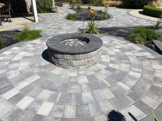 Fire Pits - We turned an empty backyard into the ultimate outdoor hangout spot by installing a custom paver patio featuring a beautiful, built-in fire pit. We worked directly with the homeowners to design an entertainment area that seamlessly flows with their yard and gives them the perfect space to gather with family and friends.
How We Built It:
Perfect Layout & Base Prep: We excavated the area and packed down a heavy-duty aggregate base, ensuring a perfectly level foundation that keeps the patio and fire pit solid and stable for years.
Heavy-Duty Fire Ring: We installed a commercial-grade steel fire ring insert to protect the stone blocks from direct heat damage, ensuring the structure stays safe and beautiful through countless bonfires.
Precision Block Work: Our crew hand-laid the retaining blocks row by row, using high-heat construction adhesive to lock the fire pit tightly into place with a crisp, seamless circular design.
Clean Finished Border: We wrapped a custom paver border around the fire pit area to accent the feature and lock the surrounding patio stones into place. Fire Pits - We turned an empty backyard into the ultimate outdoor hangout spot by installing a custom paver patio featuring a beautiful, built-in fire pit. We worked directly with the homeowners to design an entertainment area that seamlessly flows with their yard and gives them the perfect space to gather with family and friends.
How We Built It:
Perfect Layout & Base Prep: We excavated the area and packed down a heavy-duty aggregate base, ensuring a perfectly level foundation that keeps the patio and fire pit solid and stable for years.
Heavy-Duty Fire Ring: We installed a commercial-grade steel fire ring insert to protect the stone blocks from direct heat damage, ensuring the structure stays safe and beautiful through countless bonfires.
Precision Block Work: Our crew hand-laid the retaining blocks row by row, using high-heat construction adhesive to lock the fire pit tightly into place with a crisp, seamless circular design.
Clean Finished Border: We wrapped a custom paver border around the fire pit area to accent the feature and lock the surrounding patio stones into place.