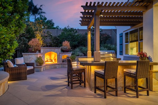 Mediterranean Inspired Home - At our client's Mediterranean-inspired Encinitas home, the garage dominated the front yard and hid their front entrance. To distract the eye from the garage doors, we designed a curved earth-tone quartzite natural stone path which was cut and laid into the existing straight-line driveway. Every plant and tree was chosen and positioned to direct the eye to the entryway. The specimen multi-trunk olive tree also provided privacy for one of the main rooms that was positioned behind the olive tree. To create additional depth, two matching wood overhang accents adjacent to the entryway’s wood overhead further complimented the entryway and the house’s architecture.
Because this couple wanted to create a space to host a constant stream of family and friends, the design allowed for numerous spaces to accommodate all of their needs. There is a custom-built fireplace, an extensive barbecue with a full bar counter area, bi-fold doors open to the main dining area, and a naturally designed spa with unique “floating” steppers that cross from the kid’s turf area to the client’s private citrus & fruit grove that the owner lovingly tends to. The spa has custom-designed height-adjusted seats for the husband and wife so that they can enjoy a full view of their backyard while relaxing. The unique LED multi-colored lights for this spa further help to create the perfect evening of enjoyment. Mediterranean Inspired Home - At our client's Mediterranean-inspired Encinitas home, the garage dominated the front yard and hid their front entrance. To distract the eye from the garage doors, we designed a curved earth-tone quartzite natural stone path which was cut and laid into the existing straight-line driveway. Every plant and tree was chosen and positioned to direct the eye to the entryway. The specimen multi-trunk olive tree also provided privacy for one of the main rooms that was positioned behind the olive tree. To create additional depth, two matching wood overhang accents adjacent to the entryway’s wood overhead further complimented the entryway and the house’s architecture.
Because this couple wanted to create a space to host a constant stream of family and friends, the design allowed for numerous spaces to accommodate all of their needs. There is a custom-built fireplace, an extensive barbecue with a full bar counter area, bi-fold doors open to the main dining area, and a naturally designed spa with unique “floating” steppers that cross from the kid’s turf area to the client’s private citrus & fruit grove that the owner lovingly tends to. The spa has custom-designed height-adjusted seats for the husband and wife so that they can enjoy a full view of their backyard while relaxing. The unique LED multi-colored lights for this spa further help to create the perfect evening of enjoyment.