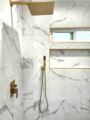 Pine Remodel - This bathroom shower features fresh white tiles with a pebble flooring, creating a clean and modern look. The satin brass trim adds a touch of elegance and complements the overall aesthetic. The dark green vanity stands out as a bold and stylish focal point, with matching satin brass sink faucets and mirrors, creating a harmonious contrast. The board and batten design on the walls adds texture and depth to the space, tying together the elements for a balanced and inviting shower area. Pine Remodel - This bathroom shower features fresh white tiles with a pebble flooring, creating a clean and modern look. The satin brass trim adds a touch of elegance and complements the overall aesthetic. The dark green vanity stands out as a bold and stylish focal point, with matching satin brass sink faucets and mirrors, creating a harmonious contrast. The board and batten design on the walls adds texture and depth to the space, tying together the elements for a balanced and inviting shower area.