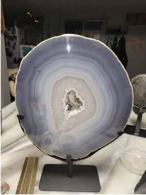 Translucent Blue Agate on a Stand - Bring a touch of tranquility and elegance to your space with our stunning Translucent Blue Agate on a Stand! This mesmerizing agate slice features beautiful shades of blue and intricate patterns that are sure to capture attention. Display it on a stand to showcase its natural beauty and enhance the energy of any room. Perfect for any metaphysical enthusiast or crystal collector, this piece is a must-have for your collection. Add a touch of spiritual energy to your home or office with this exquisite agate slice! Translucent Blue Agate on a Stand - Bring a touch of tranquility and elegance to your space with our stunning Translucent Blue Agate on a Stand! This mesmerizing agate slice features beautiful shades of blue and intricate patterns that are sure to capture attention. Display it on a stand to showcase its natural beauty and enhance the energy of any room. Perfect for any metaphysical enthusiast or crystal collector, this piece is a must-have for your collection. Add a touch of spiritual energy to your home or office with this exquisite agate slice!