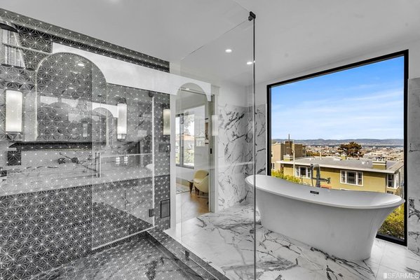 A Spa-Inspired Sanctuary with Panoramic Views - This bathroom has been reimagined into a luxurious retreat that blends modern elegance with breathtaking scenery. The centerpiece is a freestanding soaking tub positioned against a floor-to-ceiling picture window, offering uninterrupted views that create a serene, spa-like experience. Sleek marble flooring and walls bring timeless sophistication, while the walk-in shower showcases striking geometric tile work, framed by glass for an airy, open feel. Thoughtful design details, from the ambient wall sconces to the seamless flow between spaces, elevate the bathroom into a personal sanctuary where relaxation meets refined style. A Spa-Inspired Sanctuary with Panoramic Views - This bathroom has been reimagined into a luxurious retreat that blends modern elegance with breathtaking scenery. The centerpiece is a freestanding soaking tub positioned against a floor-to-ceiling picture window, offering uninterrupted views that create a serene, spa-like experience. Sleek marble flooring and walls bring timeless sophistication, while the walk-in shower showcases striking geometric tile work, framed by glass for an airy, open feel. Thoughtful design details, from the ambient wall sconces to the seamless flow between spaces, elevate the bathroom into a personal sanctuary where relaxation meets refined style.