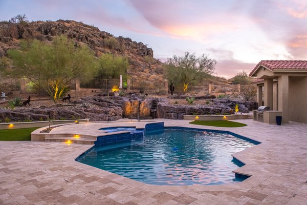 Keresan Project - Phoenix Remodel showcasing a transformed front and backyard. The homeowner wanted to update the backyard with functional decking, added features, and lighting. We provided a design with 3D renderings that checked all the boxes! Remodel Included: Baja shelf addition, pool/spa resurface, retaining walls, natural stone decking, waterfall, pavers, new softscape, synthetic turf, gravel and low voltage lighting!