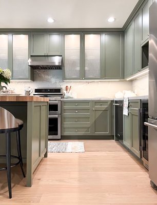 Kitchen Remodeling -  Richmond| SF - This newly remodeled kitchen features elegant sage-green cabinetry with sleek brushed metal hardware, creating a calm and stylish atmosphere. The countertops are a soft white marble with subtle grey veining, beautifully paired with a full slab backsplash that adds a touch of luxury. A standout feature is the spacious butcher block island in a rich wood tone, adding warmth and texture to the space. Stainless steel appliances, including a modern gas range and dishwasher, give the kitchen a fresh, contemporary feel. Soft under-cabinet lighting and recessed ceiling lights make the whole space feel bright, welcoming, and perfect for entertaining.
