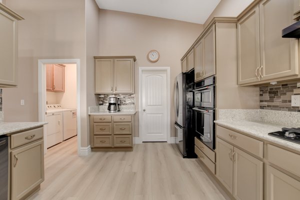 Modern Simplicity: The Gourmet Kitchen Remodel - Behold 'Modern Simplicity: The Gourmet Kitchen Remodel', a testament to timeless style and high functionality. We've reinvented this kitchen with sleek stainless steel appliances, including a state-of-the-art gas range and double ovens, sure to delight the home chef. The custom cabinetry in a soothing taupe finish harmonizes with the soft hue of the durable granite countertops. A modern mosaic tile backsplash adds depth and character, while the wide plank, light wood flooring brings a contemporary, airy feel to the room. This kitchen isn’t just a cooking space; it’s the heart of the home, reimagined for gathering, dining, and creating memories.