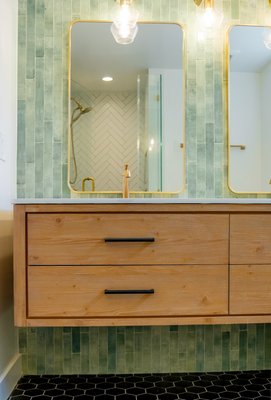Elegant Bathroom Transformation - This elegant bathroom renovation blends style and functionality. We replaced the tub with a sleek walk-in shower featuring white herringbone tiles and bold black hexagon flooring. Gold fixtures add luxury, while green wall tiles and natural wood bring warmth. A perfect balance of beauty and utility!