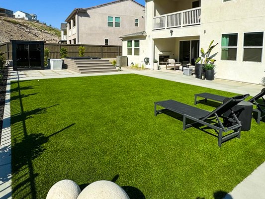 Any & Justin Full Front and Back Yard Remodel - This project involved a complete transformation of both the front and backyard of a residential property. The existing yard was an undeveloped, sloped dirt lot with poor usability and no landscaping. Our team delivered a fully integrated outdoor living space with modern design elements and functional upgrades to maximize comfort, aesthetics, and long-term value.
Scope of Work:
• Grading and site preparation
• Full artificial turf installation (front and backyard) for a clean, low-maintenance lawn
• Concrete hardscaping including walkways, steps, and a custom driveway
• Built-in spa hot tub, outdoor shower, sauna, and cold plunge tub
• Patio seating area with integrated lighting
• Custom woodwork and fencing for privacy and visual appeal
• Modern landscape lighting throughout for nighttime ambiance and safety
This outdoor renovation turned a raw and unused space into a luxurious and functional extension of the home—perfect for both everyday living and entertaining. Any & Justin Full Front and Back Yard Remodel - This project involved a complete transformation of both the front and backyard of a residential property. The existing yard was an undeveloped, sloped dirt lot with poor usability and no landscaping. Our team delivered a fully integrated outdoor living space with modern design elements and functional upgrades to maximize comfort, aesthetics, and long-term value.
Scope of Work:
• Grading and site preparation
• Full artificial turf installation (front and backyard) for a clean, low-maintenance lawn
• Concrete hardscaping including walkways, steps, and a custom driveway
• Built-in spa hot tub, outdoor shower, sauna, and cold plunge tub
• Patio seating area with integrated lighting
• Custom woodwork and fencing for privacy and visual appeal
• Modern landscape lighting throughout for nighttime ambiance and safety
This outdoor renovation turned a raw and unused space into a luxurious and functional extension of the home—perfect for both everyday living and entertaining.