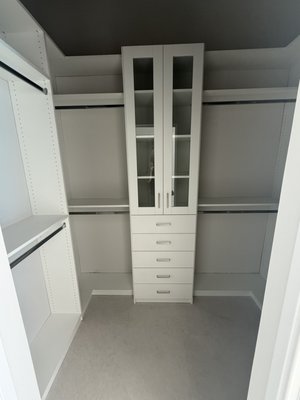 Modern White Walk-In Closet with Glass Accent Doors - This custom-designed walk-in closet maximizes storage and style with a bright, clean white finish. Featuring adjustable shelving, full-length hanging sections, and a central tower with drawers and glass accent doors, this layout brings both function and elegance to everyday organization. Sleek chrome handles and a balanced layout make it perfect for modern homes seeking a timeless, polished look. Modern White Walk-In Closet with Glass Accent Doors - This custom-designed walk-in closet maximizes storage and style with a bright, clean white finish. Featuring adjustable shelving, full-length hanging sections, and a central tower with drawers and glass accent doors, this layout brings both function and elegance to everyday organization. Sleek chrome handles and a balanced layout make it perfect for modern homes seeking a timeless, polished look.