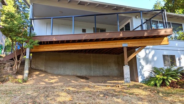 SW Portland Deck Remodel - In this project in South West Portland, our clients had a very dangerous, 50 year old deck with quite a few structural, safety and environmental protection challenges.  It was a safety hazard for anyone walking on it, due to the many rotted holes and broken boards as well as failing railings.  The deck was approximately 600 sq ft and 75 feet long.  Part of the deck ran very close to the house as well as the tree protection fence we had installed as per city code.   There was also a large tree within 4 feet of the deck perimeter which required us to collaborate closely with the Multnomah county planning and zoning department, our architect, structural engineer and our Oregon state certified arborist.   Coordinating between these stakeholders ensured we fulfilled Multnomah county’s environmental requirements.  We very carefully deconstructed the deck beams and posts to save the tree protection fence on one side and prevent damage to the house and windows on the other side.  

Once we had ensured that the new footing placement did not damage or destroy any critical roots that could cause the tree to die and fall on the house, we began to  build the new 240 sq ft deck.   In order to miss the critical root and save the tree, we had to change the new footing placement and had reduce the number of footings from 3 to 2 because of the presence of a critical root.   This required us to re-engineer a much larger and longer beam than previously used. On the deck, we used: 

Synthetic Azek grooved decking

Concealed fasteners

Alumarail railing system

The project had some additional fun and challenging structural issues with a 26' long, approximately 1400 lb beam that had to be hand carried by six craftsmen 200ft and down a 45 degree stairway for installation.  Once the beam had been moved into position, the installation of the beam required extreme precision as there was only approximately 5 inches of wiggle room.  We had to lift the beam onto the new posts without hitting the original existing post next to it that held up the roof overhead.  We had to flatten the ground and install a thick plywood base to be able use a material lift and then have six craftsmen carefully and safely guide it into position.