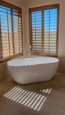 E Filaree Ln - Bathrooms remodel - This luxurious bathroom renovation showcases a modern, spa-inspired design with a focus on relaxation and elegance. The space features a sleek freestanding bathtub positioned by large windows with wooden shutters, offering stunning views of a desert landscape with mountains in the distance. A spacious walk-in shower, adorned with textured marble tiles and dual showerheads, provides a serene retreat. The shower includes a built-in bench and a handheld sprayer for added convenience. Neutral tones dominate the palette, complemented by large-format tiles and a pebble mosaic floor in the shower. Natural light floods the room, enhancing the airy ambiance, while custom cabinetry offers ample storage. A double vanity with a minimalist faucet completes the sophisticated look, blending functionality with timeless style for a tranquil, high-end bathroom experience. E Filaree Ln - Bathrooms remodel - This luxurious bathroom renovation showcases a modern, spa-inspired design with a focus on relaxation and elegance. The space features a sleek freestanding bathtub positioned by large windows with wooden shutters, offering stunning views of a desert landscape with mountains in the distance. A spacious walk-in shower, adorned with textured marble tiles and dual showerheads, provides a serene retreat. The shower includes a built-in bench and a handheld sprayer for added convenience. Neutral tones dominate the palette, complemented by large-format tiles and a pebble mosaic floor in the shower. Natural light floods the room, enhancing the airy ambiance, while custom cabinetry offers ample storage. A double vanity with a minimalist faucet completes the sophisticated look, blending functionality with timeless style for a tranquil, high-end bathroom experience.