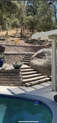 Retaining wall replacement - The existing retaining wall was leaning towards the pool so we came in and removed it. We worked with the home owners vision and a bit of our one to build this awesome 3 tiered retaining wall. We built two awesome staircases one which was shaped around the massive natural boulder. We also installed a paver patio between the top to walls for the client to hang out with his family. There are also lights under the wall caps
