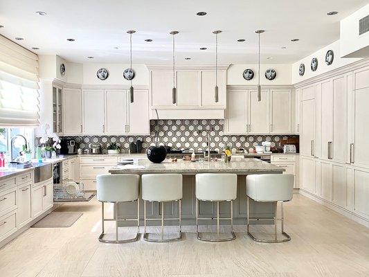Post Modern Kitchen in Newport Beach - This post-modern kitchen blends refined minimalism with expressive architectural details, creating a space that feels both structured and inviting. Clean lines and strong geometry define the overall aesthetic, while subtle decorative elements add character and visual rhythm.
The color palette is anchored in warm whites and soft neutrals, creating a bright, airy atmosphere. Light-toned surfaces are balanced with darker graphic accents in the backsplash and décor, adding contrast without overwhelming the space.
Custom cabinetry features flat-panel doors with crisp detailing, delivering a sleek, contemporary look. Integrated hardware and a streamlined layout emphasize functionality and visual continuity, while the expansive island serves as the central gathering point for cooking and entertaining.
Materials are carefully layered for depth and texture. Stone countertops provide a durable yet elegant work surface, complemented by a bold geometric tile backsplash that introduces pattern and movement. Light flooring enhances openness, while metal fixtures and modern pendant lighting add a refined, architectural finish. Post Modern Kitchen in Newport Beach - This post-modern kitchen blends refined minimalism with expressive architectural details, creating a space that feels both structured and inviting. Clean lines and strong geometry define the overall aesthetic, while subtle decorative elements add character and visual rhythm.
The color palette is anchored in warm whites and soft neutrals, creating a bright, airy atmosphere. Light-toned surfaces are balanced with darker graphic accents in the backsplash and décor, adding contrast without overwhelming the space.
Custom cabinetry features flat-panel doors with crisp detailing, delivering a sleek, contemporary look. Integrated hardware and a streamlined layout emphasize functionality and visual continuity, while the expansive island serves as the central gathering point for cooking and entertaining.
Materials are carefully layered for depth and texture. Stone countertops provide a durable yet elegant work surface, complemented by a bold geometric tile backsplash that introduces pattern and movement. Light flooring enhances openness, while metal fixtures and modern pendant lighting add a refined, architectural finish.