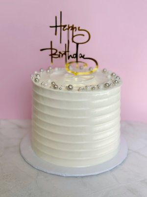 Customized Cake - This exquisite three-layered cake is 6 inches wide, adorned with smooth, velvety frosting that glistens under soft lighting. Each layer is baked to perfection, boasting a perfectly color exterior that promises a moist and flavorful interior. The top is elegantly decorated with delicate edible pearls, while the sides are finished flawlessly, showcasing the craftsmanship of the baker.