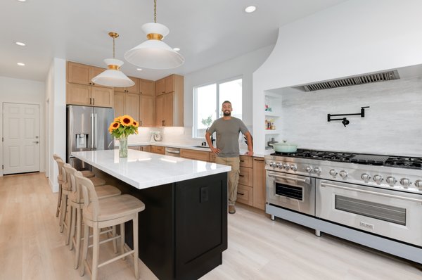 Bright & Functional Open-Concept Kitchen remodeled by Pro Builders and Design in La Costa, CA - At Pro Builders and Design, this La Costa kitchen remodel was about creating a cohesive space that feels open, functional, and elevated in everyday use. We removed dividing walls and extended the kitchen footprint to integrate naturally with the surrounding living and dining areas.
The main cabinetry is finished in a soft, wood-tone flat panel design, paired with a bold black island that serves as the centerpiece. The island features waterfall quartz countertops and includes integrated drawer storage and bar seating. To elevate both function and form, we added a suspended glass rack above the bar area. A practical touch that also serves as a visual anchor between zones.
We balanced closed storage with a row of glass-front upper cabinets, and softened the wall run with natural wood open shelving. Gold-toned hardware and pendant lighting layer in warmth against the neutral palette, without competing with the natural finishes.
Just off to the side, we placed a circular dining table that fits seamlessly within the flow of the open-concept plan, offering a defined eat-in area without interrupting movement or sightlines.
Wide-plank oak flooring runs wall-to-wall for continuity, while trimless finishes and clean ceiling lines keep the design sharp and uninterrupted.
If you're looking for a kitchen remodel that blends function, finish, and thoughtful layout, Pro Builders and Design delivers clear, design-driven results that last. Bright & Functional Open-Concept Kitchen remodeled by Pro Builders and Design in La Costa, CA - At Pro Builders and Design, this La Costa kitchen remodel was about creating a cohesive space that feels open, functional, and elevated in everyday use. We removed dividing walls and extended the kitchen footprint to integrate naturally with the surrounding living and dining areas.
The main cabinetry is finished in a soft, wood-tone flat panel design, paired with a bold black island that serves as the centerpiece. The island features waterfall quartz countertops and includes integrated drawer storage and bar seating. To elevate both function and form, we added a suspended glass rack above the bar area. A practical touch that also serves as a visual anchor between zones.
We balanced closed storage with a row of glass-front upper cabinets, and softened the wall run with natural wood open shelving. Gold-toned hardware and pendant lighting layer in warmth against the neutral palette, without competing with the natural finishes.
Just off to the side, we placed a circular dining table that fits seamlessly within the flow of the open-concept plan, offering a defined eat-in area without interrupting movement or sightlines.
Wide-plank oak flooring runs wall-to-wall for continuity, while trimless finishes and clean ceiling lines keep the design sharp and uninterrupted.
If you're looking for a kitchen remodel that blends function, finish, and thoughtful layout, Pro Builders and Design delivers clear, design-driven results that last.