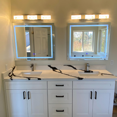 All House Bathroom Remodel - Modern bathroom vanities with a white shaker, black and white veined countertop, and illuminated LED mirrors. This space features sleek black hardware and contemporary light fixtures.