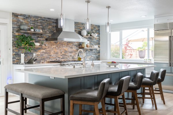 Kitchen Remodel In Placentia - This Placentia, CA kitchen was transformed from a closed‑in, dated space into an open, light‑filled entertaining hub. The original kitchen featured lowered soffits, dark appliances, and worn oak cabinetry that made the room feel small and disconnected from the rest of the home.
The remodel removed visual barriers and introduced a spacious, contemporary layout centered around a large quartz-topped island with seating for four. Custom shaker-style cabinetry in a crisp white finish provides ample storage and a clean, timeless look. Warm wood flooring and upholstered barstools add comfort and balance to the bright, modern palette.
A full-height stacked-stone feature wall with floating shelves and a professional stainless-steel hood becomes the focal point of the room, adding texture and a high-end, custom feel. Updated LED recessed lighting and clear-glass pendant fixtures evenly illuminate the space and highlight the new finishes.
The sink was relocated to the island to create a more functional work triangle and encourage interaction while cooking or entertaining. Sleek fixtures, integrated appliances, and generous counter space make everyday tasks easier and more enjoyable. Large windows and the glass patio door bring in abundant natural light and create a seamless connection to the outdoor living area.
Overall, this Placentia kitchen remodel blends modern design with practical functionality, turning an outdated room into a bright, inviting gathering place perfectly suited for both family living and entertaining. Kitchen Remodel In Placentia - This Placentia, CA kitchen was transformed from a closed‑in, dated space into an open, light‑filled entertaining hub. The original kitchen featured lowered soffits, dark appliances, and worn oak cabinetry that made the room feel small and disconnected from the rest of the home.
The remodel removed visual barriers and introduced a spacious, contemporary layout centered around a large quartz-topped island with seating for four. Custom shaker-style cabinetry in a crisp white finish provides ample storage and a clean, timeless look. Warm wood flooring and upholstered barstools add comfort and balance to the bright, modern palette.
A full-height stacked-stone feature wall with floating shelves and a professional stainless-steel hood becomes the focal point of the room, adding texture and a high-end, custom feel. Updated LED recessed lighting and clear-glass pendant fixtures evenly illuminate the space and highlight the new finishes.
The sink was relocated to the island to create a more functional work triangle and encourage interaction while cooking or entertaining. Sleek fixtures, integrated appliances, and generous counter space make everyday tasks easier and more enjoyable. Large windows and the glass patio door bring in abundant natural light and create a seamless connection to the outdoor living area.
Overall, this Placentia kitchen remodel blends modern design with practical functionality, turning an outdated room into a bright, inviting gathering place perfectly suited for both family living and entertaining.