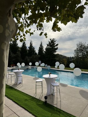 Poolside Balloon Cocktail Party - A stylish poolside cocktail setup featuring white cocktail tables, clear stools, floral accents, and floating white balloons for a modern outdoor celebration. Poolside Balloon Cocktail Party - A stylish poolside cocktail setup featuring white cocktail tables, clear stools, floral accents, and floating white balloons for a modern outdoor celebration.
