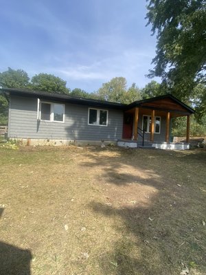 Complete porch and roofline renovation - This job was an older farm ranch style house that the homeowner was renovating top to bottom in and out. They had a grey vinyl shake siding installed and wanted to really make everything pop, with the black trim and the elegant look of natural rough sawn cedar wood to be the focal point as you drive up their long driveway. The post were replaced with 4x4 post that we wrapped with rough cedar and custom trim at the top and bottom of post. The beveled rough cedar siding being installed on the front gable gives the house a unique 1 of a kind sharp look. The concrete slab was pretty beat up so with a grinder we smoothed out the really bad imperfections and filled in the big cracks before painting a non-slip epoxy paint on top surface. The entire roofline of the house was covered in black aluminum trim and soffit to protect all the new wood we installed. Then we installed new black gutters to round off the look and protect the foundation.