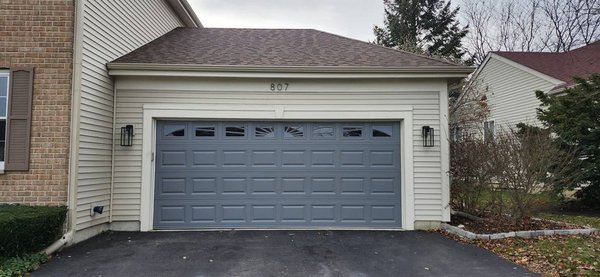 Classic Detail: Graphite Raised Panel with Sunburst Windows - We upgraded a sectional door with a Raised Short Panel design in a bold graphite finish, topped with elegant sunburst window inserts. A timeless look with character and charm.