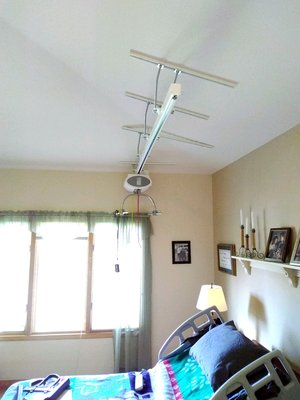 Overhead Ceiling Lift System - This overhead ceiling lift system was installed over a disabled person's bed. The track motor is what lifts a person, and it can be remote controlled to glide on the track system custom installed on this vaulted ceiling. This lift system allows a person to safely and more easily transfer between a bed and chair, and back. It alleviates the lifting typically involved with body transfers, sparing a caregiver's back. Overhead Ceiling Lift System - This overhead ceiling lift system was installed over a disabled person's bed. The track motor is what lifts a person, and it can be remote controlled to glide on the track system custom installed on this vaulted ceiling. This lift system allows a person to safely and more easily transfer between a bed and chair, and back. It alleviates the lifting typically involved with body transfers, sparing a caregiver's back.
