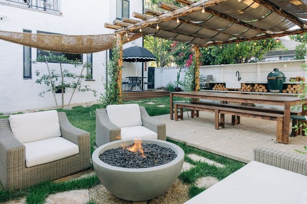 Outdoor Living Designed for Gathering | Short-Term Rental Backyard Transformation - Some outdoor spaces are beautiful. Others become the reason people come back.

Our clients approached us with a vision to transform their short-term rental into more than just another place to stay. They wanted an outdoor living space that would create memorable experiences—a destination where families could gather, friends could reconnect, meals could last for hours, and guests would leave with memories that extended far beyond the property itself.

Every design decision centered around how people would experience the space.

A custom natural log pergola serves as the heart of the landscape, creating a warm, inviting outdoor dining area designed for large gatherings. Throughout the day, filtered sunlight moves across the dining table, while evenings are transformed by dimmable bistro lighting that creates a relaxed, Tuscan-inspired atmosphere.

To create both beauty and functionality, we designed a combination of paver patios and stamped, stained concrete walkways that naturally guide guests through the yard. Rather than feeling like separate features, each outdoor space flows seamlessly into the next, encouraging people to explore, relax, and spend time together outdoors.

Natural materials were selected to create warmth and timeless character. Trex decking provides a durable, low-maintenance entertaining space, while natural tan flagstone set within grass softens the hardscape and creates visual interest. Gravel pathways, mulch, and thoughtfully layered planting beds add texture while helping the landscape feel established and connected to its surroundings.

The lawn was intentionally kept open to provide flexibility. Children have room to play, families can spread out for lawn games or picnics, and guests always have space to gather without the yard feeling crowded.

Planting design balanced beauty with long-term practicality. Espalier fruit trees provide seasonal interest and architectural structure while maximizing usable space. California-friendly, drought-conscious plantings reduce maintenance and water use while creating a lush, welcoming landscape. A carefully selected privacy hedge adds a sense of retreat without making the yard feel enclosed.

As part of the overall landscape design, we also collaborated with the client's broader vision by thoughtfully integrating future outdoor features, including an outdoor kitchen, fire pit, water feature, and additional shade structures. Planning these elements early helped ensure the final landscape feels cohesive, intentional, and built to evolve over time.

This project reflects our design-build approach at Herencia Landscaping. We believe exceptional landscapes begin with understanding how people want to live outdoors. Every project is thoughtfully designed around our clients' lifestyle, blending craftsmanship, functionality, and natural beauty into spaces that invite connection.

The completed backyard feels warm, timeless, and welcoming—reminiscent of the relaxed charm of the Tuscan countryside while remaining perfectly suited for Southern California living.

More than a landscape, this is a place where conversations linger, celebrations happen naturally, and guests leave feeling refreshed, connected, and eager to return. That's the kind of outdoor living experience we strive to create with every project.

If you're looking for a landscape contractor specializing in custom backyard transformations, outdoor living spaces, landscape design, paver patios, pergolas, drought-tolerant landscaping, or complete design-build landscaping, we'd love to help bring your vision to life.