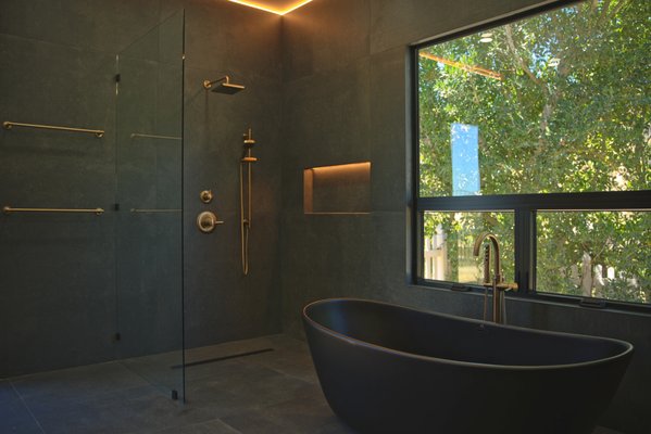 Master Bathroom Remodel - This custom primary bathroom remodel in Poway, CA transforms a standard bathroom into a sleek, spa-inspired modern sanctuary. Designed around moody color palettes, clean architectural geometry, and warm ambient lighting, the project seamlessly combines dark slate-toned tile with natural wood elements and luxury brushed brass fixtures.
Design Highlights & Key Features
Statement Soaking Tub: A matte black freestanding vessel tub paired with a floor-mounted brushed brass tub filler positioned to capture outdoor views.
Custom Walk-In Shower: High-contrast, dark-tiled frameless glass enclosure featuring a rainfall showerhead, hand sprayer, and built-in LED-illuminated recessed niche.
Modern Vanity & Custom Lighting: Warm natural wood vanity topped with dark solid-surface countertops, paired with sleek gold faucets and hanging architectural cylinder pendant lights.
Seamless Luxury: Full-height dark wall tile, organic textures, and premium water-efficient fixtures throughout. Master Bathroom Remodel - This custom primary bathroom remodel in Poway, CA transforms a standard bathroom into a sleek, spa-inspired modern sanctuary. Designed around moody color palettes, clean architectural geometry, and warm ambient lighting, the project seamlessly combines dark slate-toned tile with natural wood elements and luxury brushed brass fixtures.
Design Highlights & Key Features
Statement Soaking Tub: A matte black freestanding vessel tub paired with a floor-mounted brushed brass tub filler positioned to capture outdoor views.
Custom Walk-In Shower: High-contrast, dark-tiled frameless glass enclosure featuring a rainfall showerhead, hand sprayer, and built-in LED-illuminated recessed niche.
Modern Vanity & Custom Lighting: Warm natural wood vanity topped with dark solid-surface countertops, paired with sleek gold faucets and hanging architectural cylinder pendant lights.
Seamless Luxury: Full-height dark wall tile, organic textures, and premium water-efficient fixtures throughout.
