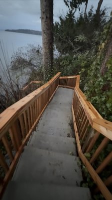 Port Orchard Waterfront Beach-Access Concrete Stairs - A private beach-access stairway down a steep waterfront bluff in Port Orchard, WA — engineered footings and rebar-tied formwork stepped down the slope, a poured-in-place concrete stair, and a cedar handrail system leading right down to the Puget Sound shoreline.

Scope as general contractor: terracing the bluff and building rebar-tied forms that step the stair safely down the grade; a monolithic, broom-finished concrete stair poured in place for a durable, low-maintenance run; a code-height cedar railing on both sides; cutting, shoring and re-planting the bank so the new stair sits stable on the waterfront slope.

The challenge: safe, lasting beach access down a steep Puget Sound bluff is all about structure and drainage. Continuous steel in stepped forms and a monolithic pour give the owners a stair they can walk comfortably from the yard to the shoreline for decades.

Permitted through the City of Port Orchard / Kitsap County. About two weeks on site. The photos follow the stair from formwork and rebar through the pour to the finished cedar-railed run.