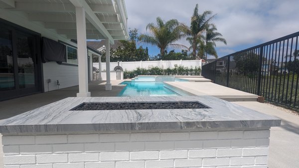 Pool Remodel in Laguna Niguel - Our latest masterpiece showcases a complete overhaul, including a pristine pool and spa remodel, integrating modern elegance with unparalleled comfort.
1. Pool and Spa Revitalization:
- Replastered and Retiled: Witness the stunning metamorphosis of your pool and spa, adorned with exquisite glass tiles and a smooth, durable white plaster finish that promises both beauty and longevity.
- Enhanced Lighting: Experience enchanting evenings by the poolside, thanks to newly installed energy-efficient LED lights illuminating your pool and spa in a mesmerizing glow.
- Leak Repairs: Rest easy knowing that our experts meticulously repaired any leaks in your spa, ensuring its functionality and restoring its integrity.
2. Tanning Shelf Addition:
- Relaxation Redefined: Indulge in tranquility on your new tanning shelf, basking under the sun while enjoying the gentle caress of the water—a perfect spot for unwinding in the comfort of your own backyard.
3. Modern Poured-in-Place Concrete Coping:
- Elevated Elegance: Out with the old, in with the new! The traditional brick coping has been replaced with sleek poured-in-place concrete, adding a touch of modern sophistication to your pool's edges.
4. Stylish Outdoor Kitchen:
- Culinary Delights: Elevate your outdoor dining experience with a fully loaded kitchen featuring a high-performance grill, a pizza oven for gourmet creations, a convenient mini fridge, and ample storage for all your culinary essentials.
5. Custom Built White Brick Fire Pit:
- Warmth and Style: Embrace the cozy ambiance of your custom-built white brick fire pit, crowned with a luxurious quartzite top. It’s not just a source of warmth but also a striking focal point that enhances the visual appeal of your outdoor area.
6. Washed Finish Concrete Decking:
- Understated Elegance: Your outdoor space now features washed finish concrete decking, providing a clean and contemporary backdrop that beautifully complements the surrounding elements.
At Custom Pro Construction, we don't just remodel backyards; we craft immersive experiences tailored to your desires. Let our portfolio inspire your own outdoor dreams. Contact us today and let’s transform your backyard into a sanctuary of luxury and relaxation. Your oasis awaits! Pool Remodel in Laguna Niguel - Our latest masterpiece showcases a complete overhaul, including a pristine pool and spa remodel, integrating modern elegance with unparalleled comfort.
1. Pool and Spa Revitalization:
- Replastered and Retiled: Witness the stunning metamorphosis of your pool and spa, adorned with exquisite glass tiles and a smooth, durable white plaster finish that promises both beauty and longevity.
- Enhanced Lighting: Experience enchanting evenings by the poolside, thanks to newly installed energy-efficient LED lights illuminating your pool and spa in a mesmerizing glow.
- Leak Repairs: Rest easy knowing that our experts meticulously repaired any leaks in your spa, ensuring its functionality and restoring its integrity.
2. Tanning Shelf Addition:
- Relaxation Redefined: Indulge in tranquility on your new tanning shelf, basking under the sun while enjoying the gentle caress of the water—a perfect spot for unwinding in the comfort of your own backyard.
3. Modern Poured-in-Place Concrete Coping:
- Elevated Elegance: Out with the old, in with the new! The traditional brick coping has been replaced with sleek poured-in-place concrete, adding a touch of modern sophistication to your pool's edges.
4. Stylish Outdoor Kitchen:
- Culinary Delights: Elevate your outdoor dining experience with a fully loaded kitchen featuring a high-performance grill, a pizza oven for gourmet creations, a convenient mini fridge, and ample storage for all your culinary essentials.
5. Custom Built White Brick Fire Pit:
- Warmth and Style: Embrace the cozy ambiance of your custom-built white brick fire pit, crowned with a luxurious quartzite top. It’s not just a source of warmth but also a striking focal point that enhances the visual appeal of your outdoor area.
6. Washed Finish Concrete Decking:
- Understated Elegance: Your outdoor space now features washed finish concrete decking, providing a clean and contemporary backdrop that beautifully complements the surrounding elements.
At Custom Pro Construction, we don't just remodel backyards; we craft immersive experiences tailored to your desires. Let our portfolio inspire your own outdoor dreams. Contact us today and let’s transform your backyard into a sanctuary of luxury and relaxation. Your oasis awaits!
