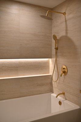 Soft Stone Bath Remodel | Elevate Builders Hawaii - This bathroom remodel was designed with warm stone-look tile, brushed brass fixtures, a lit shower niche, and a custom floating wood vanity. The space feels soft, refined, and comfortable, with details that bring a quiet spa-like feeling into everyday routines. Soft Stone Bath Remodel | Elevate Builders Hawaii - This bathroom remodel was designed with warm stone-look tile, brushed brass fixtures, a lit shower niche, and a custom floating wood vanity. The space feels soft, refined, and comfortable, with details that bring a quiet spa-like feeling into everyday routines.