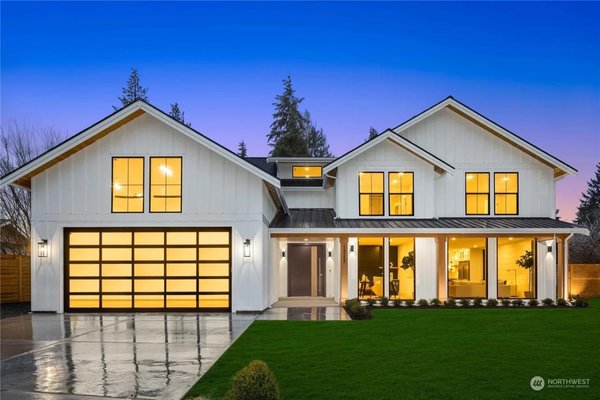 Bellevue New Construction — 4,500 sq ft Modern Farmhouse - Ground-up modern farmhouse in Bellevue, WA — 4,500 sq ft, 5 bedrooms, 4.5 baths — built where a worn-out rambler once stood. ID Builder Construction handled the project end to end as the general contractor: demolition of the existing house, clearing and grading, the new foundation, two-story framing with floor-to-ceiling window walls, board-and-batten siding, a standing-seam metal porch roof, black-frame glazing and a glass-panel garage door.

Inside: a dramatic two-story black-slat feature wall with an open-riser steel stair and cable rail, wide-plank white-oak floors, a designer kitchen with custom cabinetry, quartz counters and brass fixtures, a glass-enclosed LED-lit wine display, a marble primary bath with a black herringbone double shower, a Hollywood-style makeup vanity room, walk-in closet, home theater, paneled rec room and office — all opening through a wall of glass to a fully fenced, freshly sodded backyard.

The challenge: the double-height stair and slat wall. Steel stringers, open treads and cable rail all had to land within tight tolerances against the glazing behind them, so framing, steel and finish carpentry were sequenced by our own crews to read as one continuous sculptural piece.

Permitted through the City of Bellevue. 10 months from permit to completion. The photos follow the build from the original rambler through demolition, framing and dry-in to the finished home.