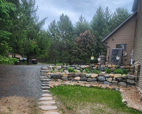 Two tier boulder retaining wall with a rock stair case - Customer needed the dirt retained along the side of the house to prevent wash outs. They also wanted a stair case to get up and down the hill easier and we spread gravel next to the stair case so they could drive their lawnmower or UTV's or whatever, up and down the hill. Two tier boulder retaining wall with a rock stair case - Customer needed the dirt retained along the side of the house to prevent wash outs. They also wanted a stair case to get up and down the hill easier and we spread gravel next to the stair case so they could drive their lawnmower or UTV's or whatever, up and down the hill.