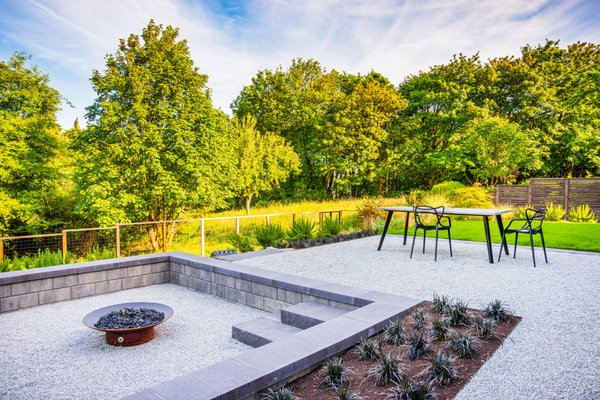 Modern in the Country - Bordering a beautiful greenspace at the edge of town, the clean lines of this modern landscaped contrasts beautifully with the native trees. A unique and relatively affordable option of salt and pepper granite gravel was framed in by metal edging to create a clean and inviting patio and walkway surfaces. Belgard Tandem Walls add to the modern style and one-piece concrete steps create function and beautiful access to the various rooms in the backyard. Altogether, this well-designed backyard is evidence again that sometimes less is more. Modern in the Country - Bordering a beautiful greenspace at the edge of town, the clean lines of this modern landscaped contrasts beautifully with the native trees. A unique and relatively affordable option of salt and pepper granite gravel was framed in by metal edging to create a clean and inviting patio and walkway surfaces. Belgard Tandem Walls add to the modern style and one-piece concrete steps create function and beautiful access to the various rooms in the backyard. Altogether, this well-designed backyard is evidence again that sometimes less is more.