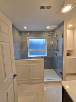 Portage Park- Bathroom Remodel - This project featured a complete bathroom remodel and reconfiguration to enhance both functionality and aesthetics. The original layout included a jacuzzi tub and a leaking shower pan. Our team expanded the usable space and installed a custom walk-in shower, Quartz windowsill, and a hidden quartz niche. The design includes custom batten board wall detailing, marble floor tile, all complemented by with blue shower wall tiles. To complete the space, we installed a beautiful oak vanity paired with three stylish sconces, and white shaker style top / bottom shelving for extra storage.