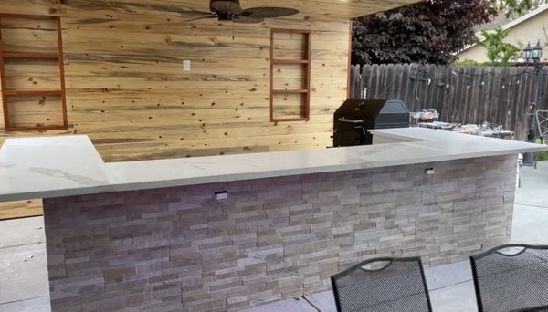 Milpitas - Outdoor kitchen with over hand that included Recessed lighting + a ceiling fan and outlet to power tv on the wall next to the custom shelving made out of redwood to add accent and space to decorate the room. Functional fridge and outlets on the bar side along with under lighting on the bar edge.